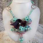 Collier Blue Flowers brodé avec un ruban de soie framboise/truffe à laquelle s’ajoute : cabochons, perles nacrées Rosaline et Ivoire, toupies Jet, anneaux ovales, perles marbrées Bleu Ciel et Blanc